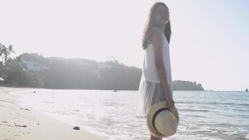 Chica sujetando sombrero de paja de pie en la playa bajo la luz del sol video