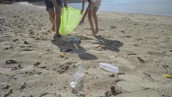 Madre e hija recogiendo residuos de botellas de plástico en la playa de arena video
