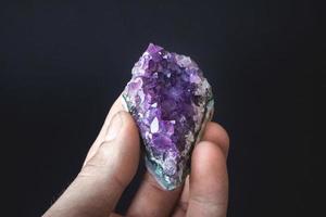 Cristal violeta de amatista en la palma de la mano sobre un fondo negro foto