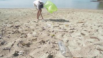 jovem coletando lixo na praia em um saco plástico verde