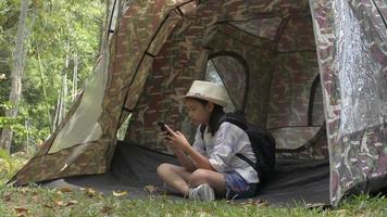 fille avec sac à dos assise et utilisant un téléphone portable devant la tente video