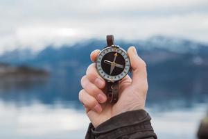 mano sostiene la brújula contra el fondo de la montaña y un lago foto