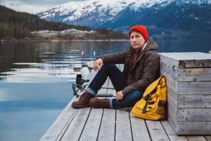 Traveler man sitting on wooden pier on the background of mountain photo