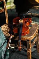 Primer plano de un violín con un arco en una silla de madera en la luz del sol foto