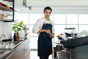 asian barista using coffee grinder machine to gride coffee beans photo