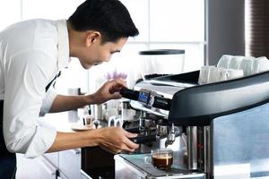 Joven barista asiático preparar café de la máquina cafetera en el café