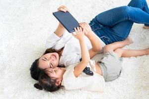 asian mother watching cartoon in tablet with young child at home photo