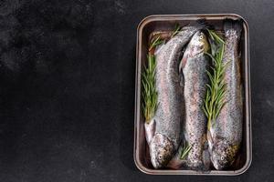 Raw trout lie on a black stone chopping board on a dark concrete table photo