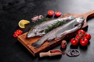 Raw trout lie on a black stone chopping board on a dark concrete table photo