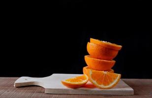 Orange slices on wooden cutting board on black background photo