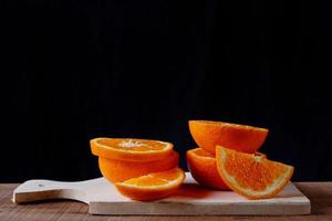 Rodajas de naranja sobre tabla de cortar de madera sobre fondo negro foto