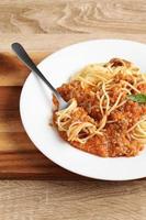 Close up a fork with spaghetti and red sauce in dish photo