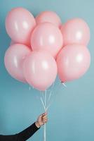 Pink air flying balloons in man hands isolated on blue background photo