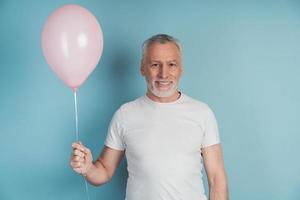 Happy retired man in white t-shirt holding pink balloon photo