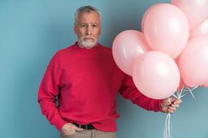 Upset, older bearded man wears, holding balloons in his hand photo