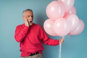 Surprised, the older man holds pink balloons in his hand photo