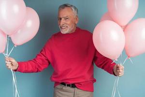 Photo of an attractive, senior man holding pink balloons