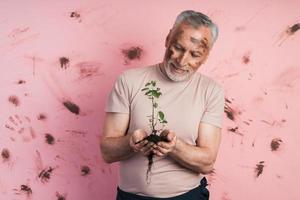 Elderly, gray-haired man with a beard holds a plant in his hands