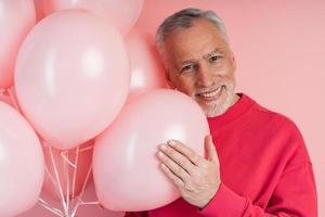 Positive, cheerful man with balloons posing on pink wall background photo