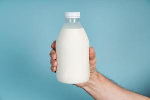 Male hand holds a bottle of milk on a blue background photo
