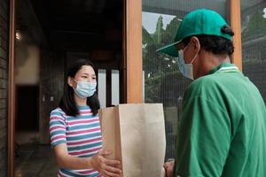 Delivery man with face mask gives parcel to an Asian woman. photo