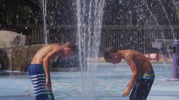 Children playing in water fountains on summer day, slow motion video