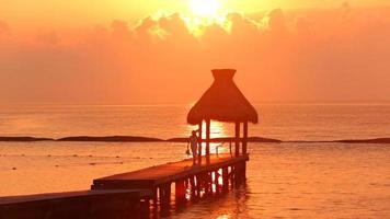 Mujer camina por el muelle durante la puesta de sol en el resort tropical video