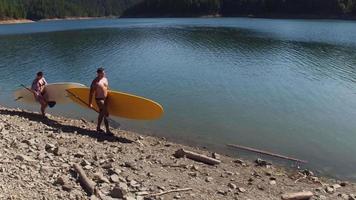 Couple walking by lake with stand up paddle boards video