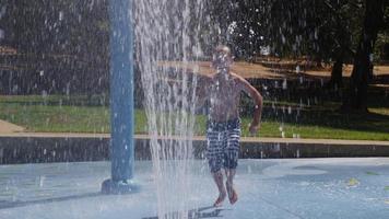 Boy jumping through water fountain on summer day, slow motion video