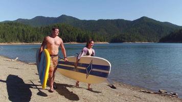 Couple walking by lake with stand up paddle boards video