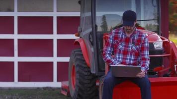 Farmer sits on tractor using laptop computer video