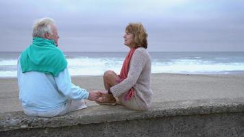 Senior couple sitting on wall at beach together video