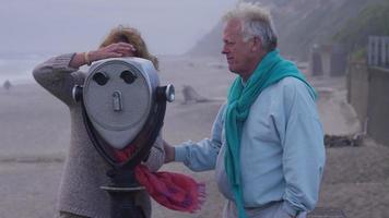 senior koppel op het strand kijkend door de kijker video