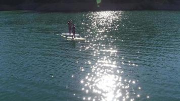 Aerial drone shot of couple paddling stand up paddle boards on lake video