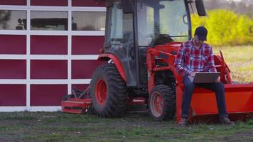 Farmer sits on tractor using laptop computer video