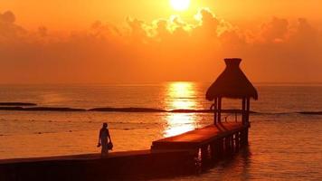 la donna cammina lungo il molo durante il tramonto al resort tropicale video