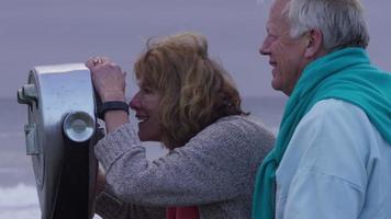 Las parejas ancianas en la playa mirando a través del visor video