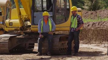 dos trabajadores de pie junto a la excavadora video