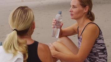 Two women resting and drinking water after run. video