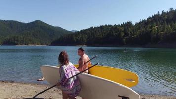 paar wandelen langs het meer met opstaande paddleboards? video