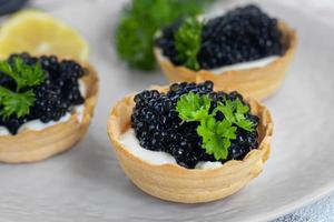 Black caviar in tartlets on a light background. Healthy food concept. photo