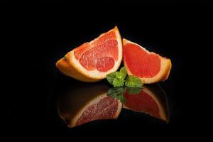 Slices of grapefruit on a dark background with a sprig of mint.