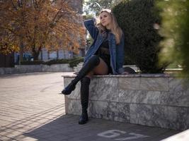 Joven rubia con hermosas piernas largas con botas se sienta en la calle foto