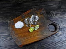 Dos tragos de plata de tequila con limón fresco y sal marina sobre tabla de madera