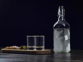 Botella de vodka, dos vasos empañados con vodka frío sobre una tabla de madera