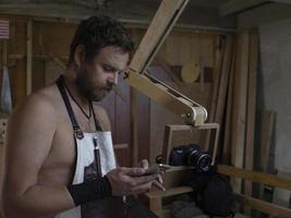 A MAN WITH A BEARD IN AN APRON ON A BARE BODY LOOKS AT THE PHONE photo