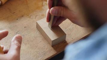 carpenter cuts a square hole on the board with a chisel