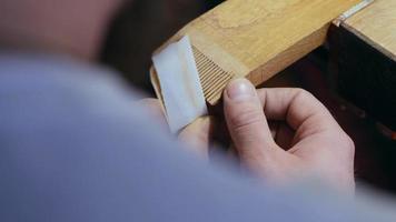 woodworker grinds teeth on a wooden comb with sanding paper