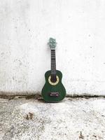 A green ukulele leaning against white wall photo