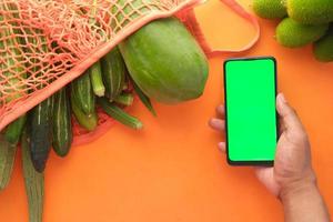 Vista superior de la mano del hombre sosteniendo un teléfono inteligente con verduras frescas foto